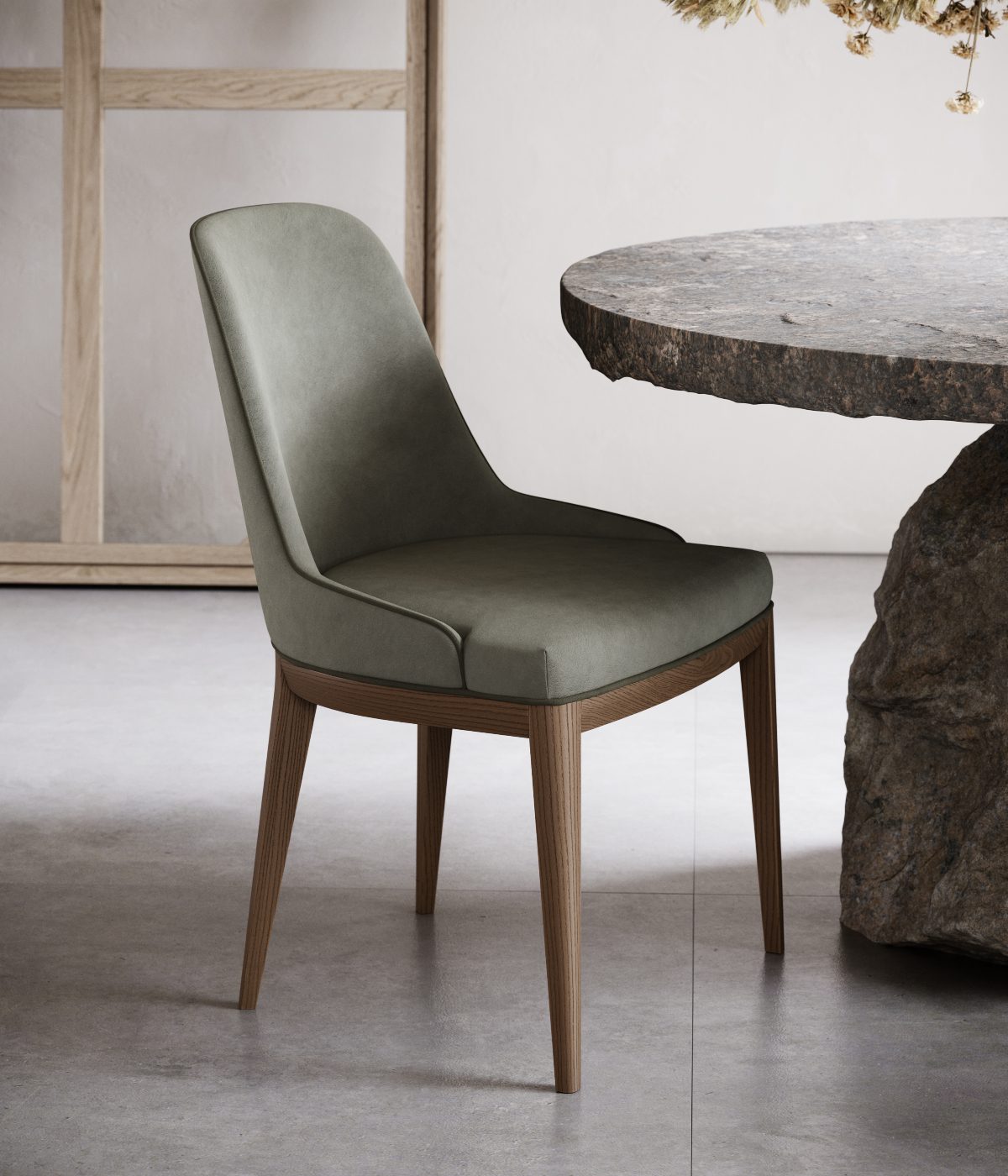 Anna chair without armrests 2022 A green-upholstered chair located in front of a stone table, offering a comfortable spot for relaxation or dining.