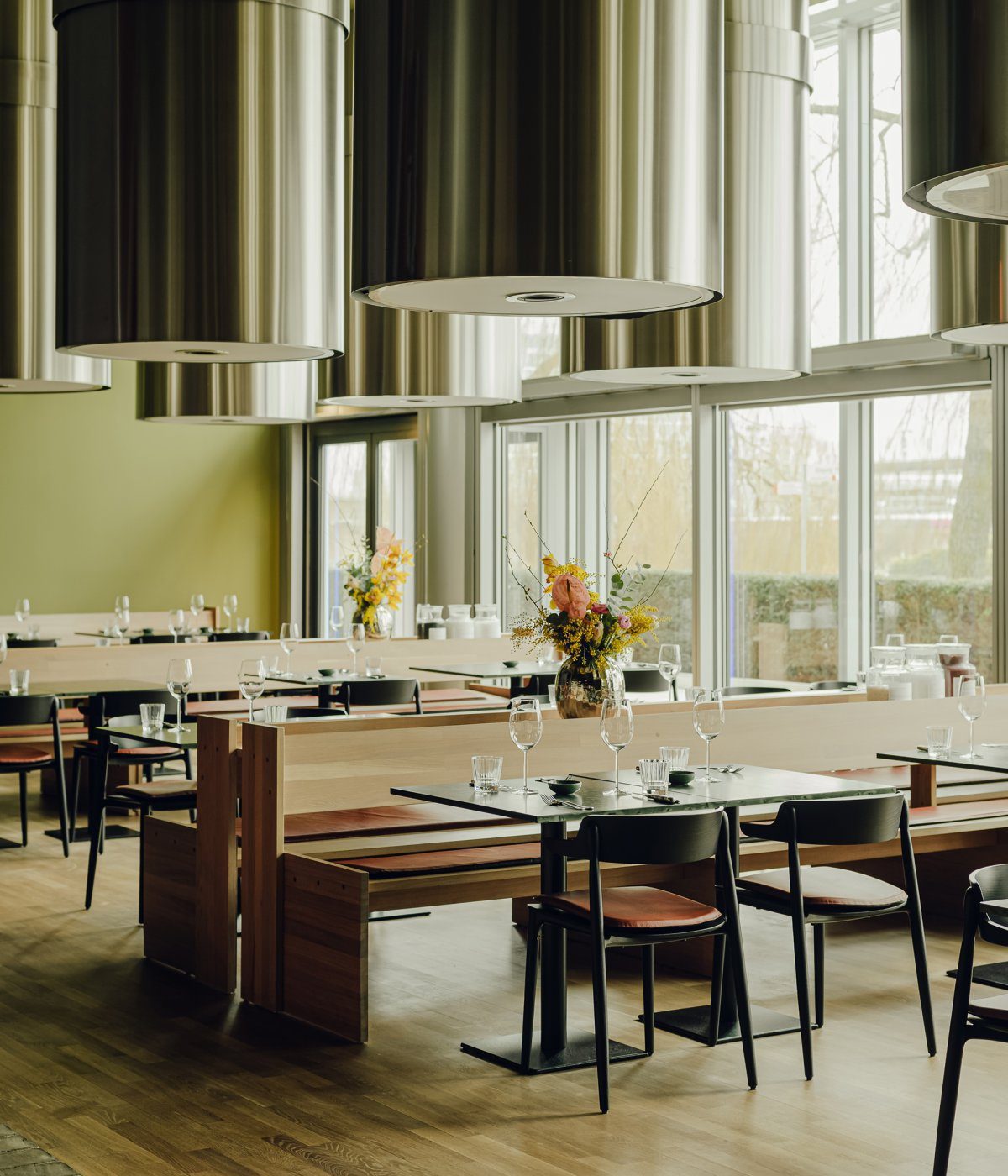 Beefclub-Restaurant-by-Ester-Bruzkus-Architekten (1) Restaurant with metal chandelier on the ceiling and wood furniture. The dining chairs are in black and there are wood benches.