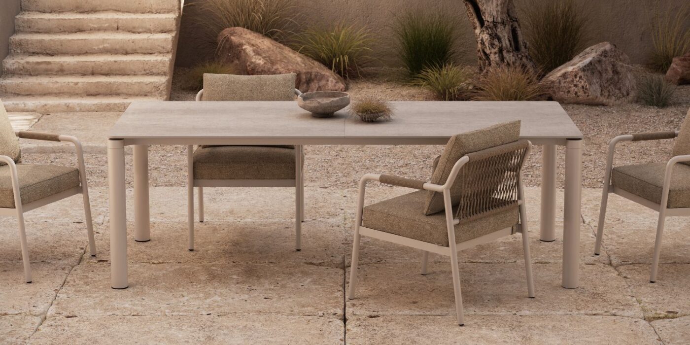 Blog Featured Image - 2026-05-14T165419.174 Outdoor patio with a minimalist design features a rectangular table and four chairs on a stone surface. Succulents and rocks add a natural touch.