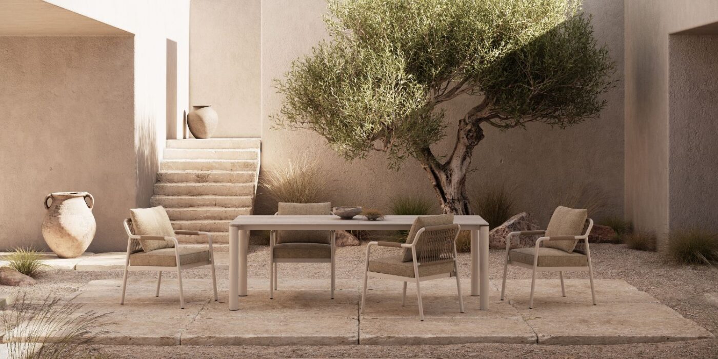 Blog Featured Image - 2026-05-19T163057.055 Minimalist outdoor patio with a rectangular table, five cushioned chairs, and an olive tree. Warm beige tones and pottery evoke a serene, Mediterranean vibe.