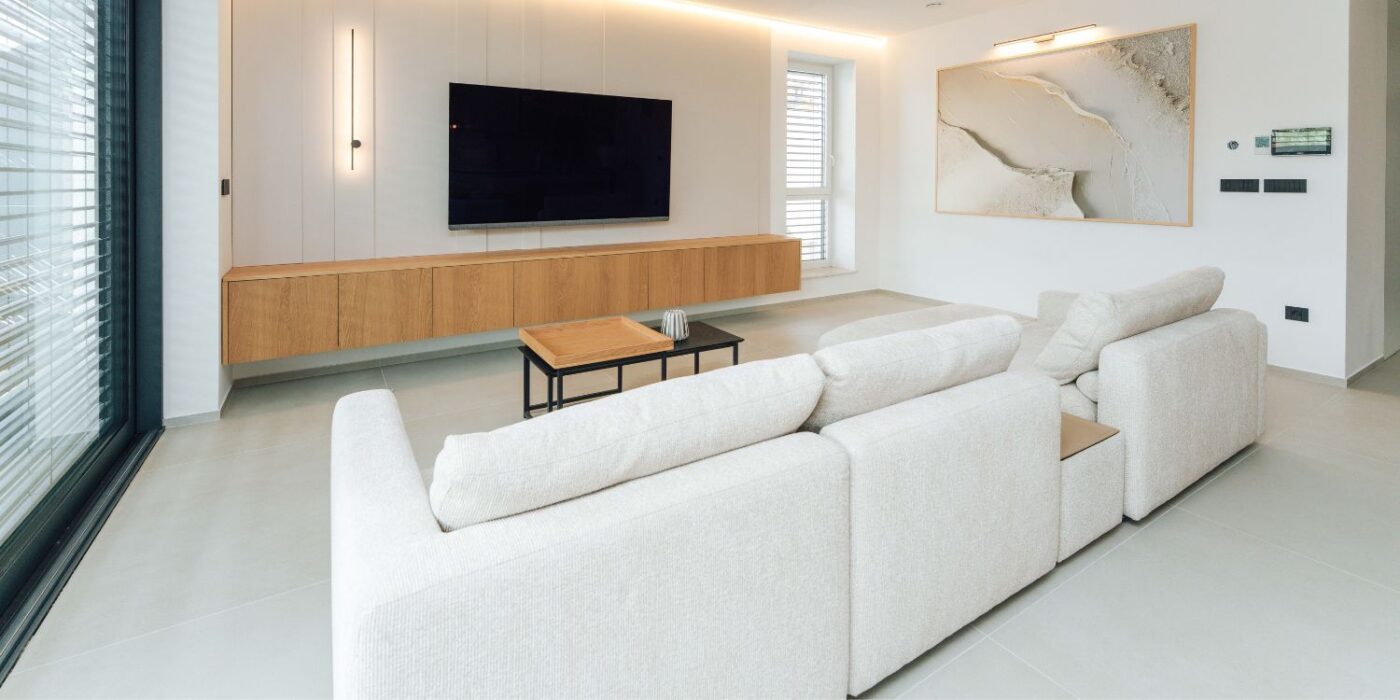 A modern living room featuring white furniture and a flat-screen TV on the wall.