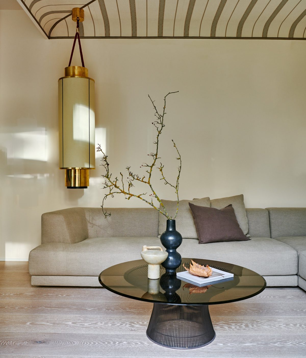 Carlo Berlin Project (1) Living room in a modern aesthetic. With a round and long chandelier in gold and beige. The sofa is in beige and has a coffee table in the centre in black and glass. By one of the best interior designers in germany - Carlo Berlin.