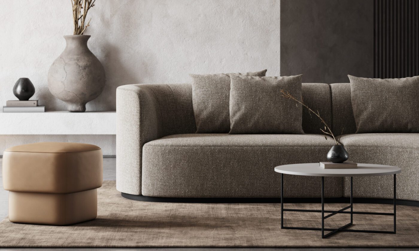 Chloe sofa winter A modern living room with a beige sofa adorned with three cushions, a round coffee table with a small vase, and a tan ottoman. A large, textured vase and decorative objects are on a white shelf in the background. Neutral colors and minimalist design. Interior Design Trends For Winter
