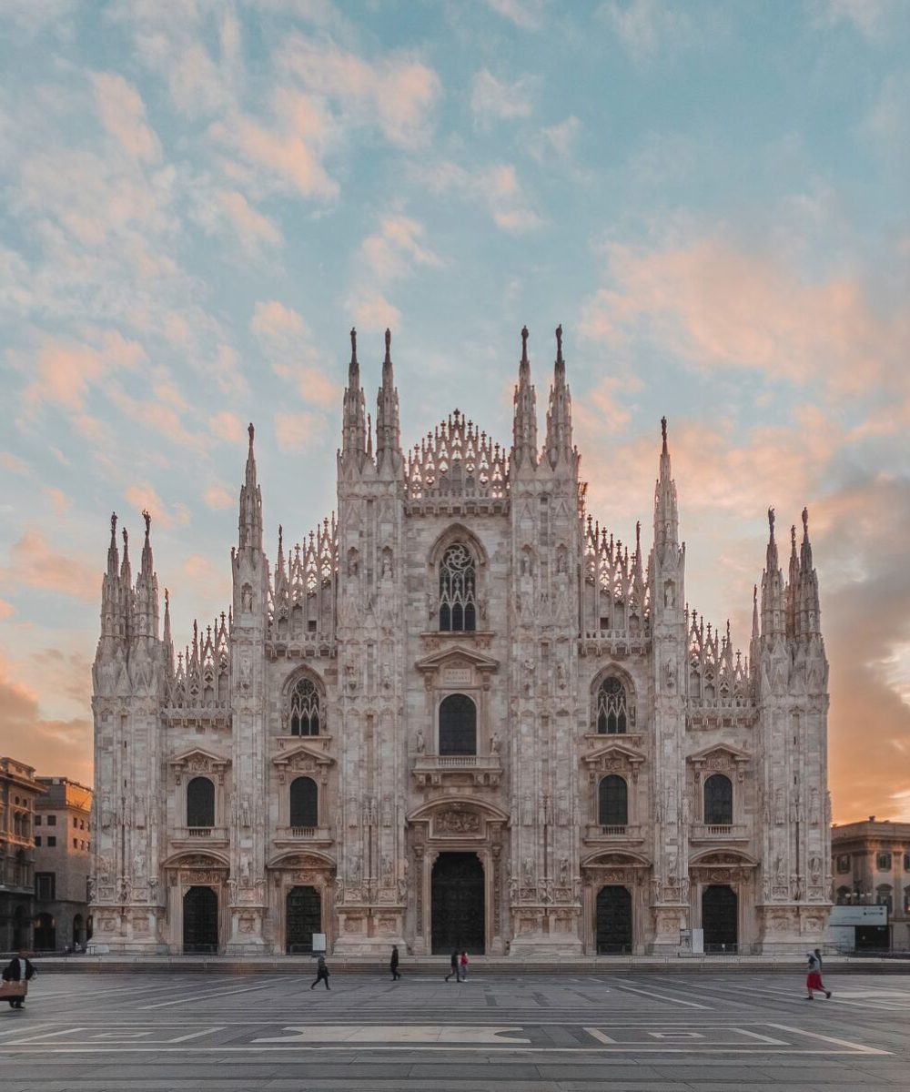 Duomo Di Milano (1) The stunning Duomo in Milan, Italy, showcasing its intricate Gothic architecture and towering spires against a clear blue sky.