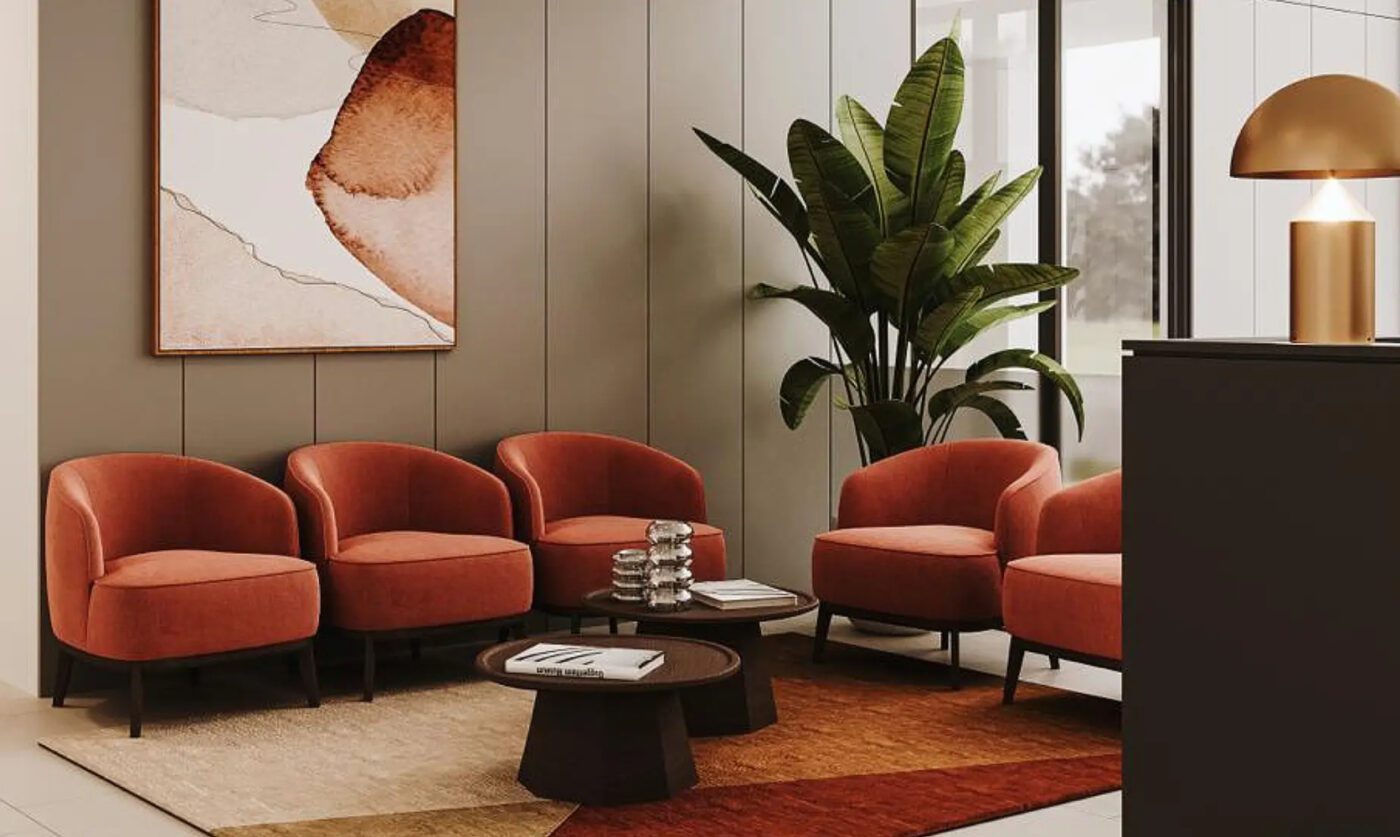 Fabiia Project lobby project with five armchairs in peach colour and two wood coffee tables at the centre. With a vase with a green plant in the back and a piece of art in neutral tones. On the floor is a rug in terracotta and neutral tones.