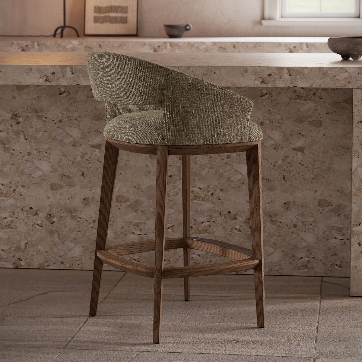 Jermain Bar Chair by Domkapa (1) A modern bar chair with a textured fabric seat and curved backrest sits in front of a terrazzo counter. Muted tones create a calm, minimalist ambiance.