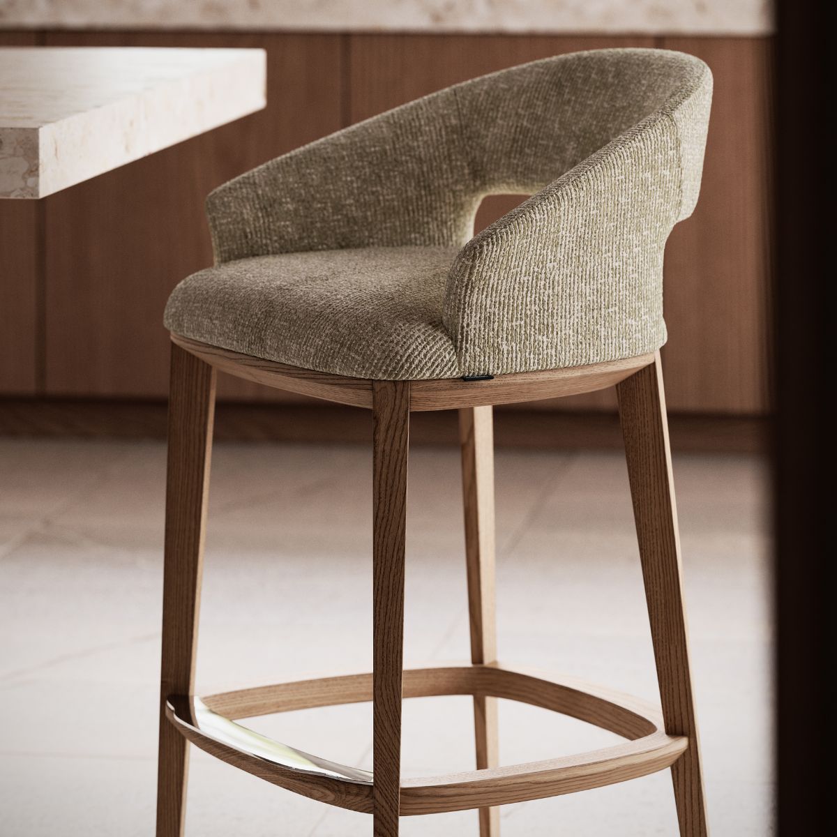 Jermain Bar Chair by Domkapa A modern bar chair with a textured green fabric seat and wooden legs is beside a marble-topped counter, set against a warm-toned, minimalist interior.