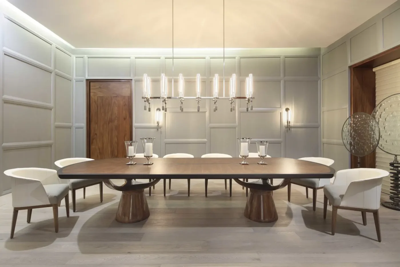 Modern dining room with a large wooden table, eight white chairs, and a sleek chandelier. Neutral colours create a calm and elegant atmosphere.