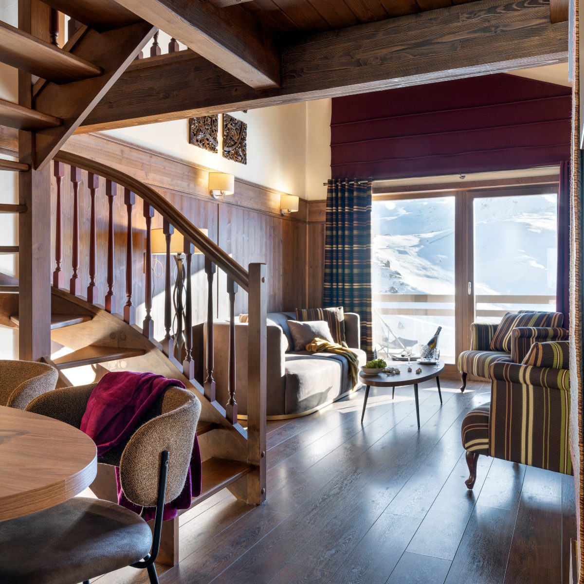 Le Hameau du Kashmir Suite Prestige Cosy wooden stairs leading up in a warm, inviting room filled with natural light. A suite from the Le Hameau du Kashmir, a hotel in the French Alps.