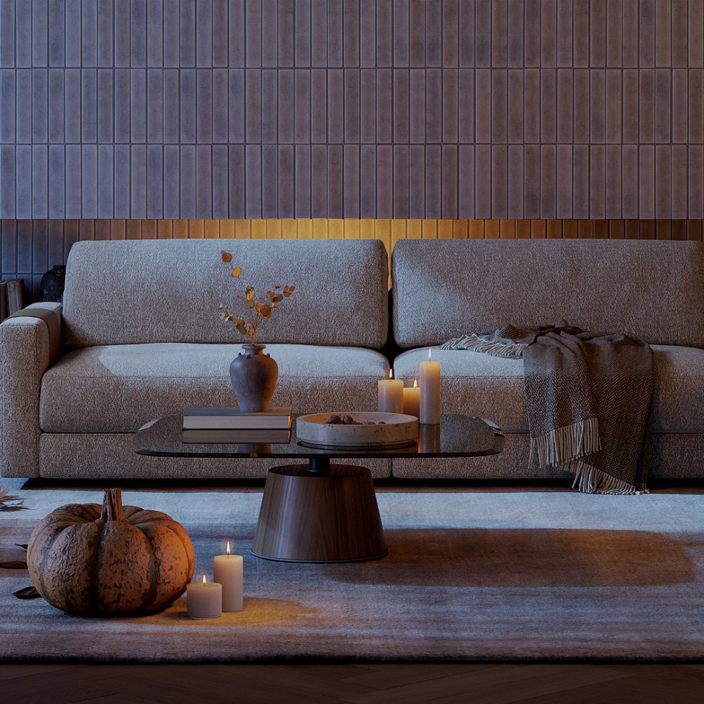 Living room with halloween accents A cosy living room with a beige sofa and a modern coffee table. The table features a vase with dried foliage, stacked books, and lit candles. A pumpkin is placed on the floor beside the table. A soft throw blanket is draped over the sofa.