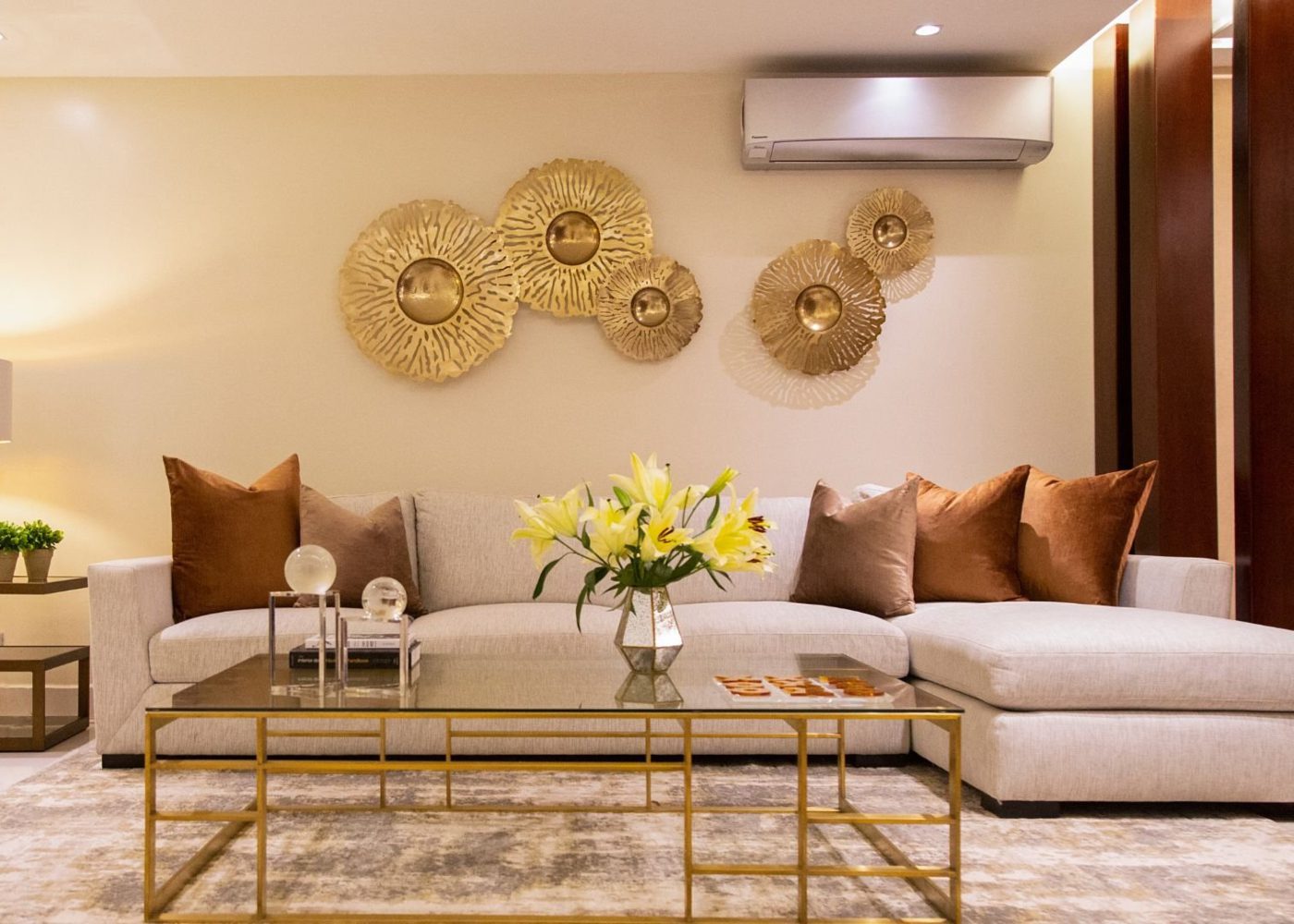 Love Design Panama Living room in neutrals with gold accents. With a beige sofa and two brown armchairs. In the centre is a square coffee table with gold metal and the top in dark glass.
