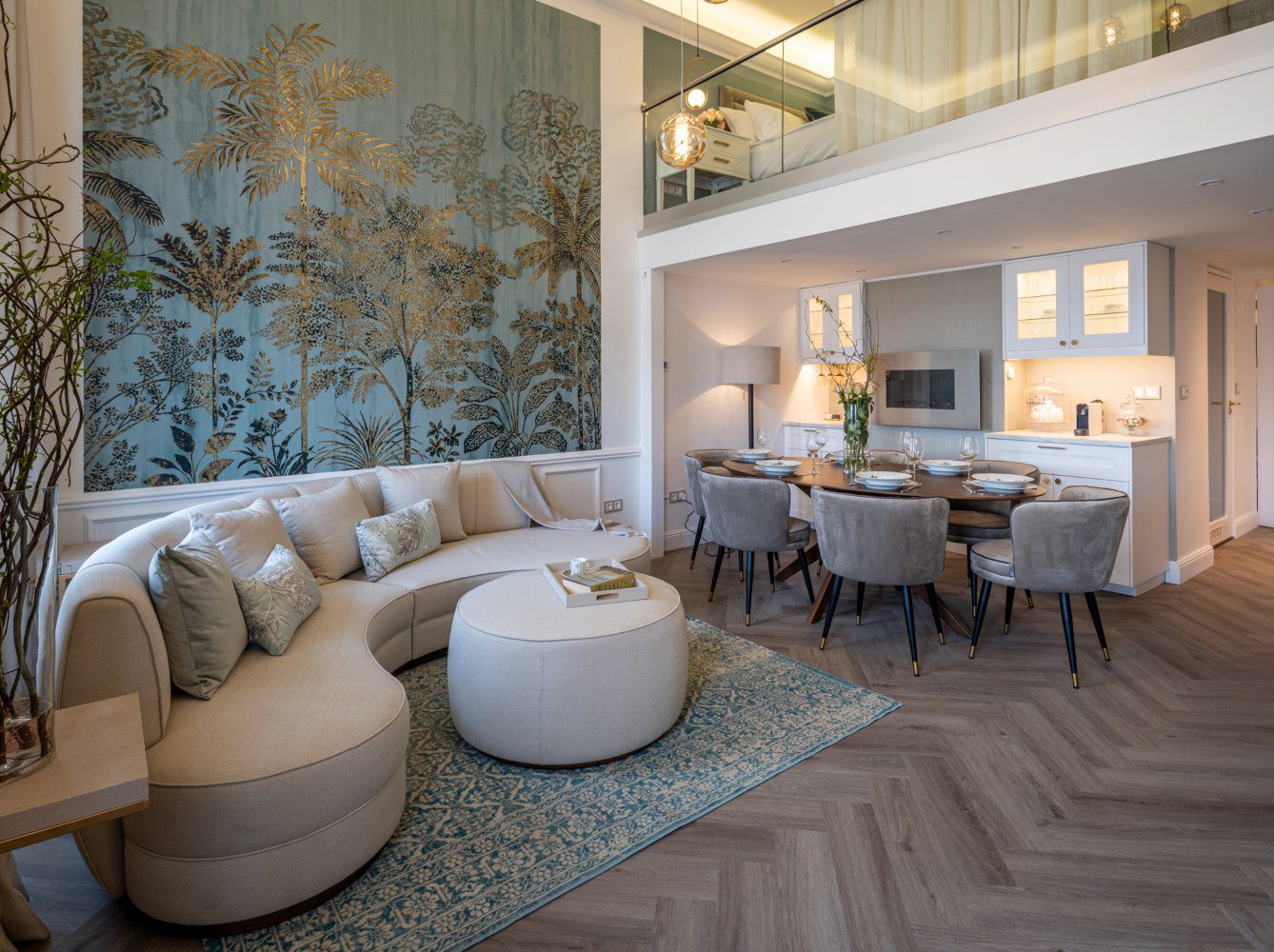 Luxury Airbnb apartment by La Fenice Interiors Living room and dining room with a white sofa, white pouf, oval dining table and six brown dining chairs. With a wall with a blue print and gold accents.