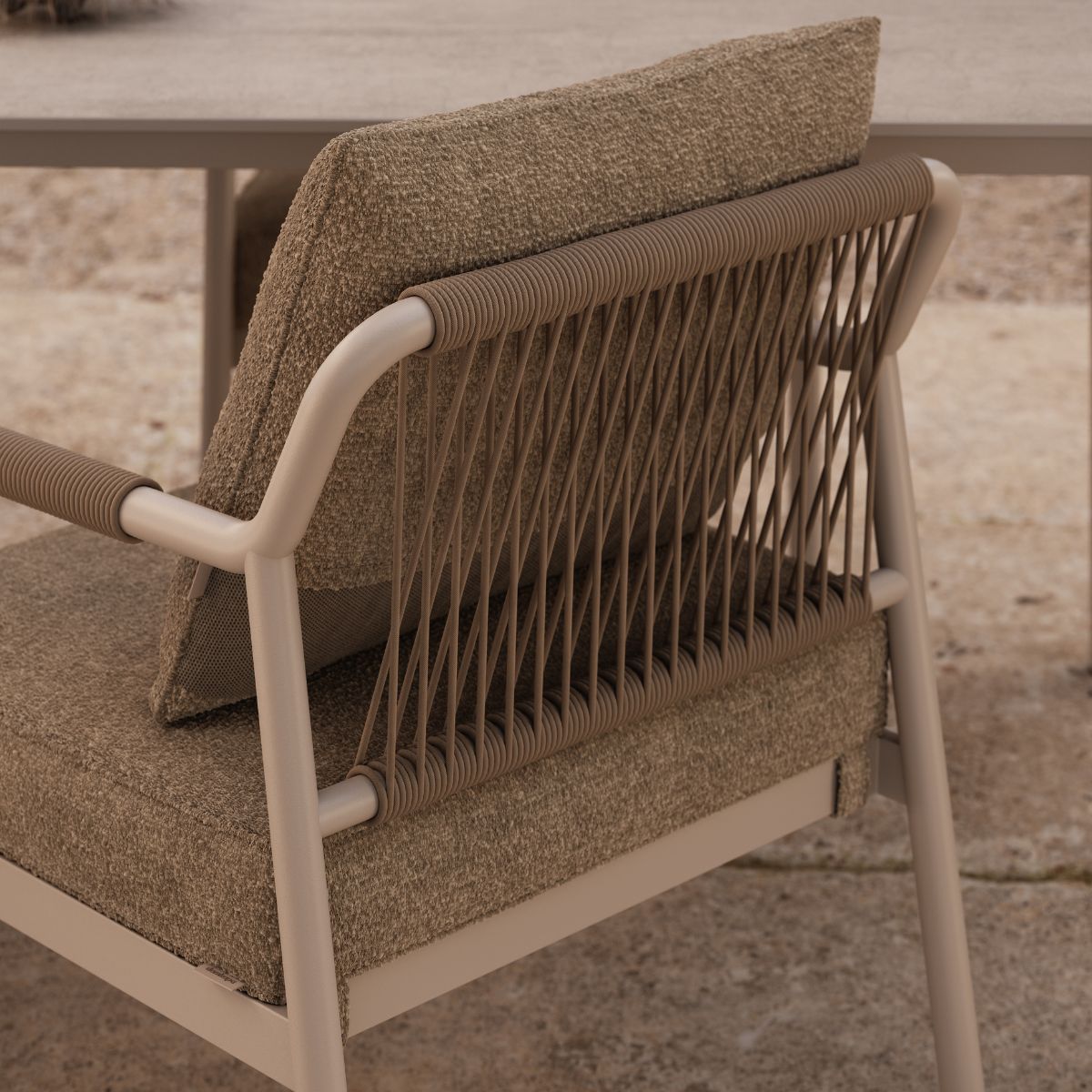 Neroli Dining Chair by Domkapa (1) Close-up of a beige outdoor chair with textured cushions and a woven backrest. The chair sits on stone tiles, evoking a calm, rustic feel.