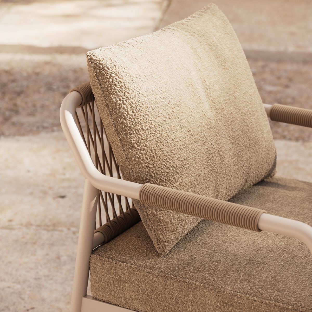 Neroli Dining Chair by Domkapa (2) Close-up of a beige cushioned outdoor chair with textured fabric and tubular armrests. The setting is sunlit, creating a warm and inviting tone.