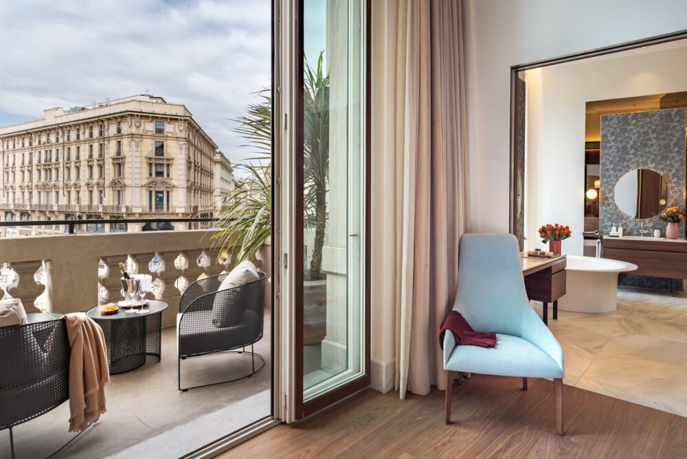 Palazzo Cordusio 3 Bright bedroom with a panoramic window showcasing a vibrant cityscape outside.