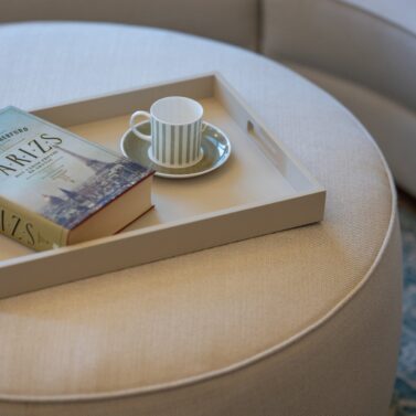 Rachel Pouf in La Fenice Interiors Project (1) Rachel pouf in white with a book and a coffee cup on top.
