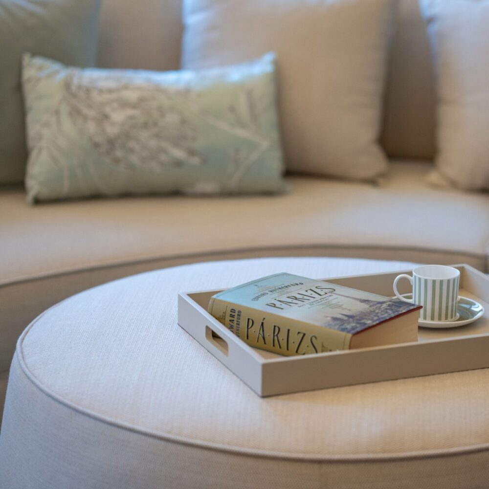 Rachel Pouf in La Fenice Interiors Project (2) Rachel pouf in white with a book and a coffee cup on top.