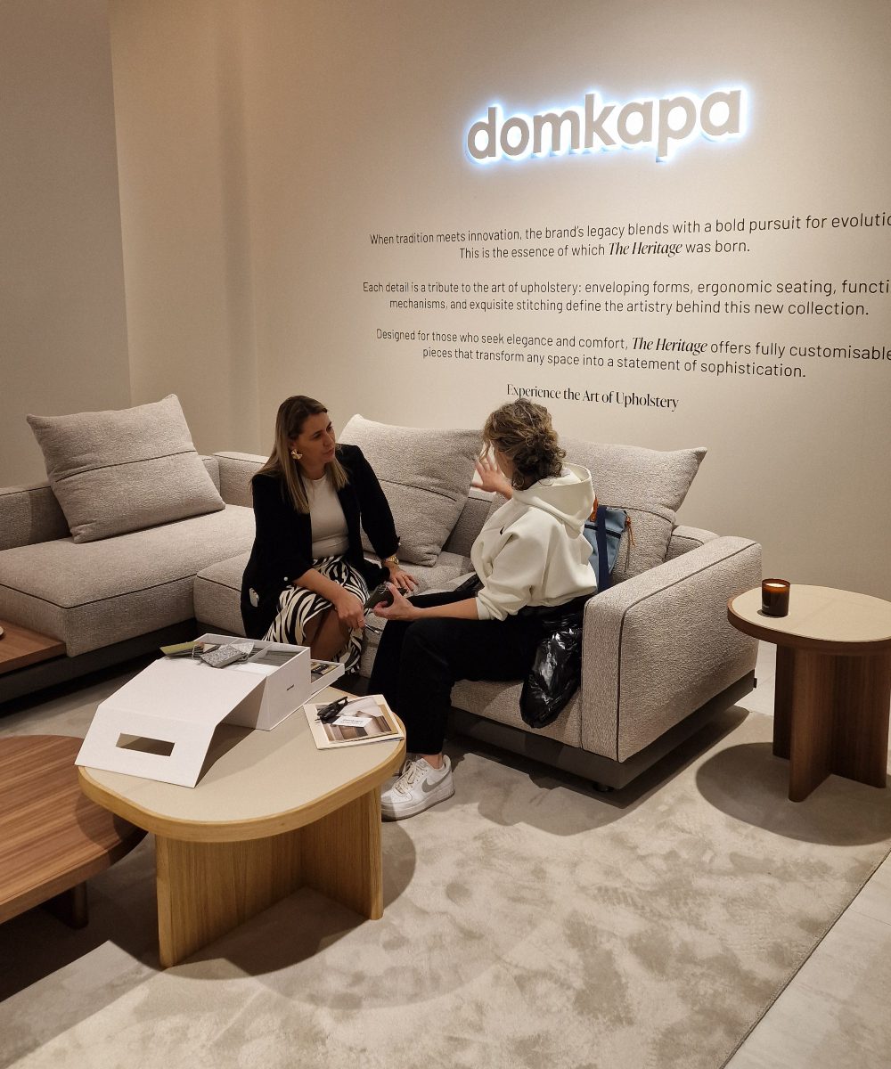 Sample box selection with client Two women sit comfortably on a sofa, with a "Domkapa" sign visible behind them. They are discussing a project and selection the materials with the help of a sample box.
