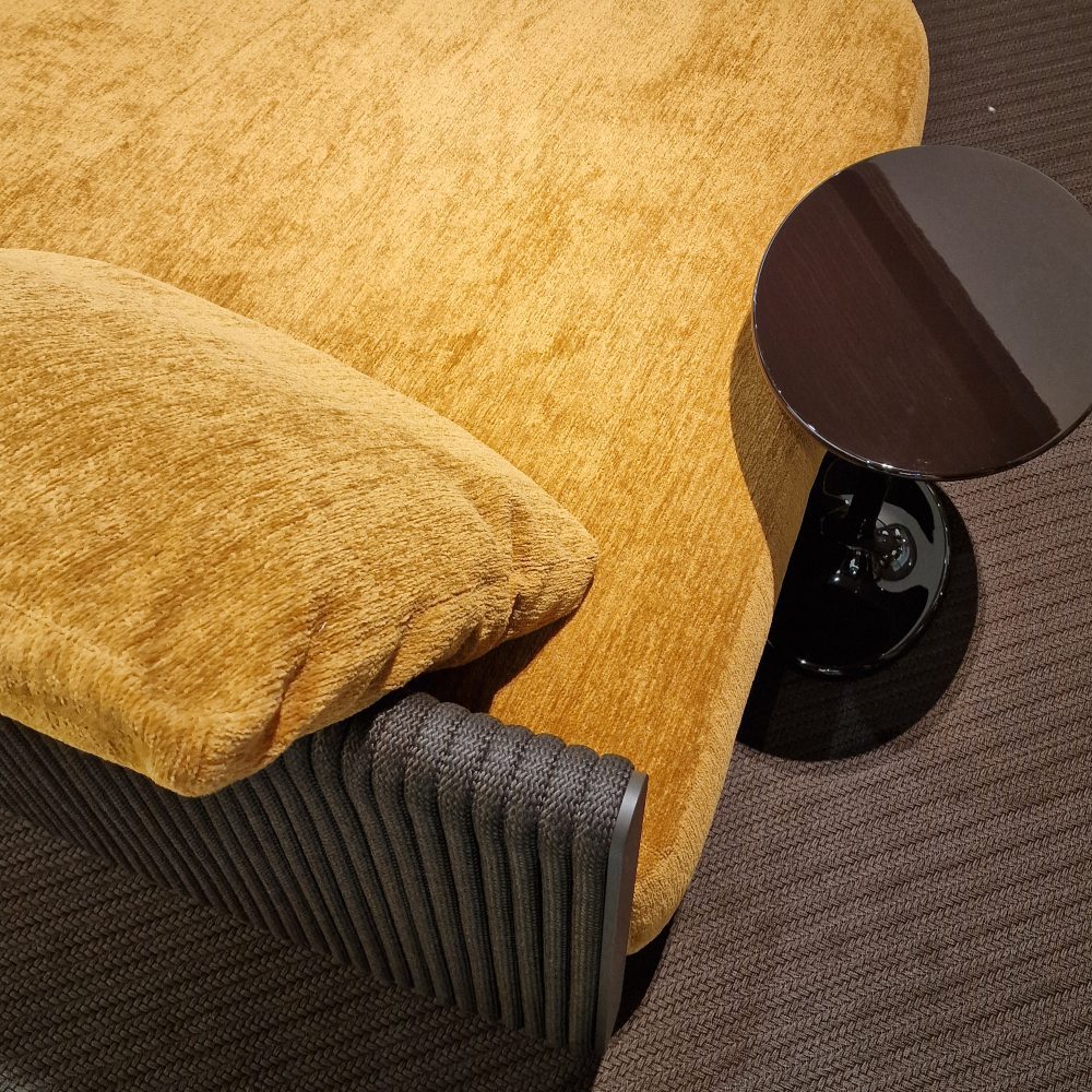 Earth toned sofa upholstered in fabric. With a lacquered side table. Seen at salone del mobile 2025.