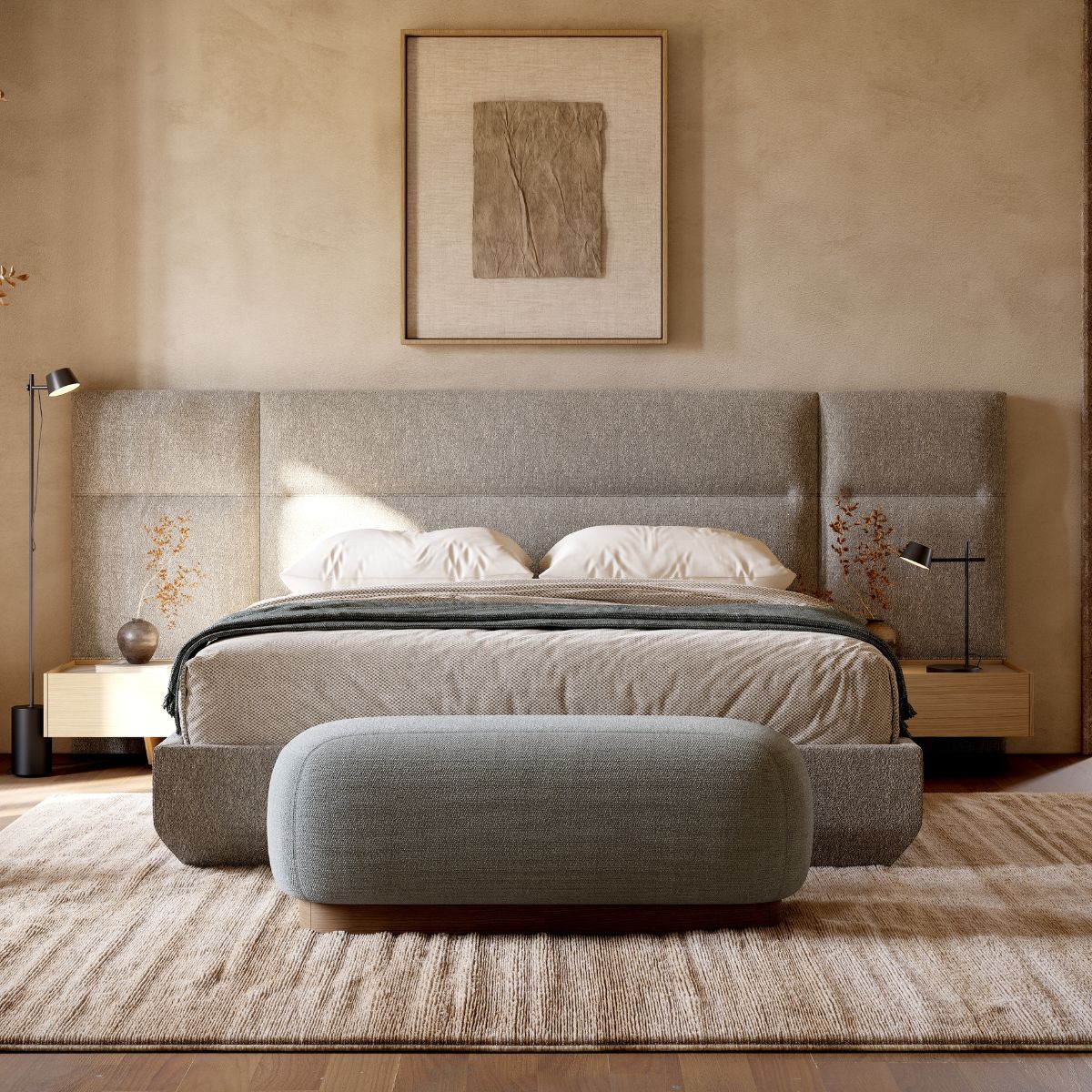 A minimalist bedroom features a neutral-toned upholstered bed with a large cushioned headboard. A textured bench sits on a soft rug, with gentle lighting creating a serene atmosphere. Above the bed hangs abstract art framed in wood.
