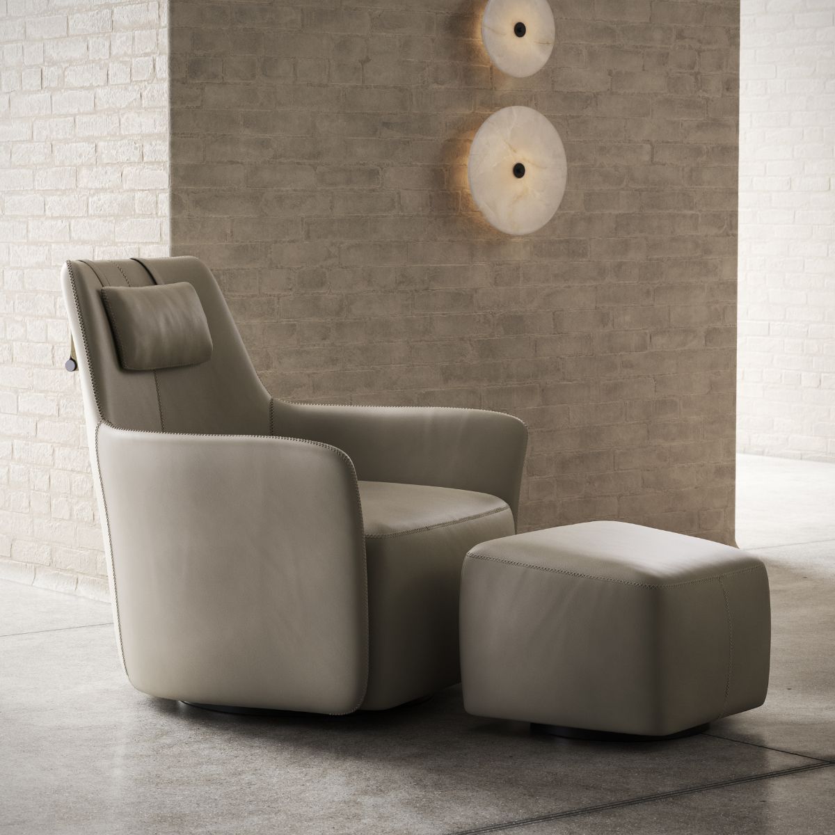 A modern beige armchair with a matching ottoman sits on a concrete floor against a brick wall. Two round wall lights provide ambient lighting.