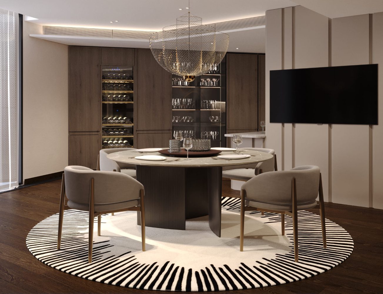 5 Influentional Interior Designers In The UK - UB London A modern dining room with a round table surrounded by four chairs on a patterned rug. A wine cabinet and shelves with glassware are in the background. A large chandelier hangs from the ceiling, and a flat-screen TV is mounted on the wall.