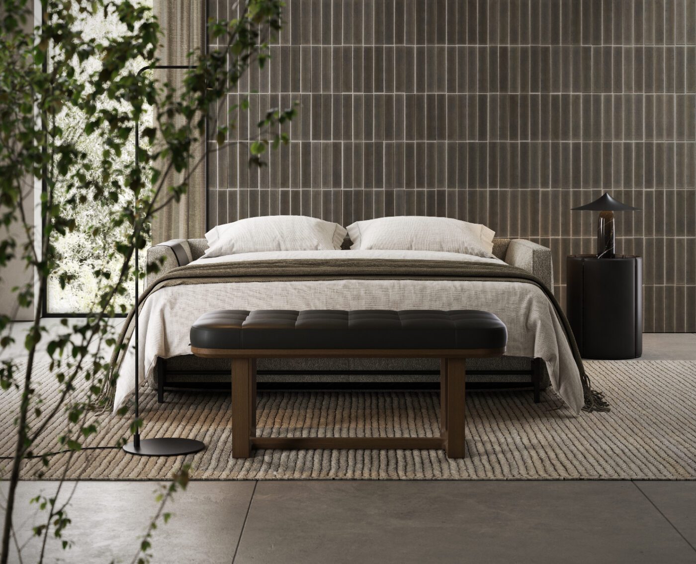Vincent Bench A modern bedroom with a neatly made bed, white pillows, and a dark gray blanket. A wooden bench is at the bed's foot, and a small round table with a lamp is on the side. A plant is in the foreground, and vertical tile walls and a large window are visible.