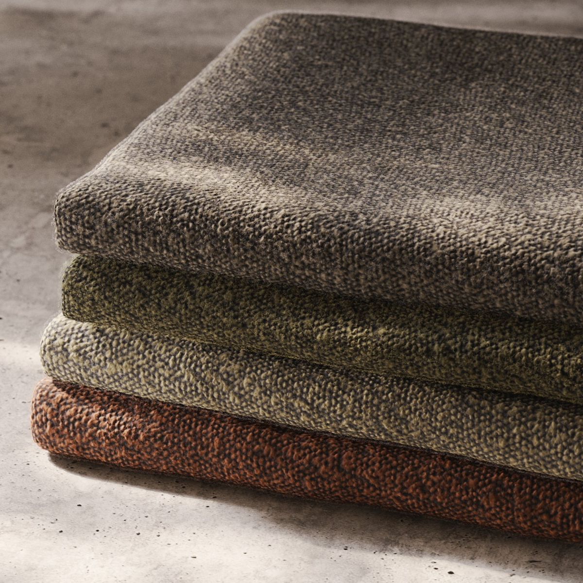 A stack of four neatly folded fabric swateches resting on a concrete floor. COM vs. house fabric