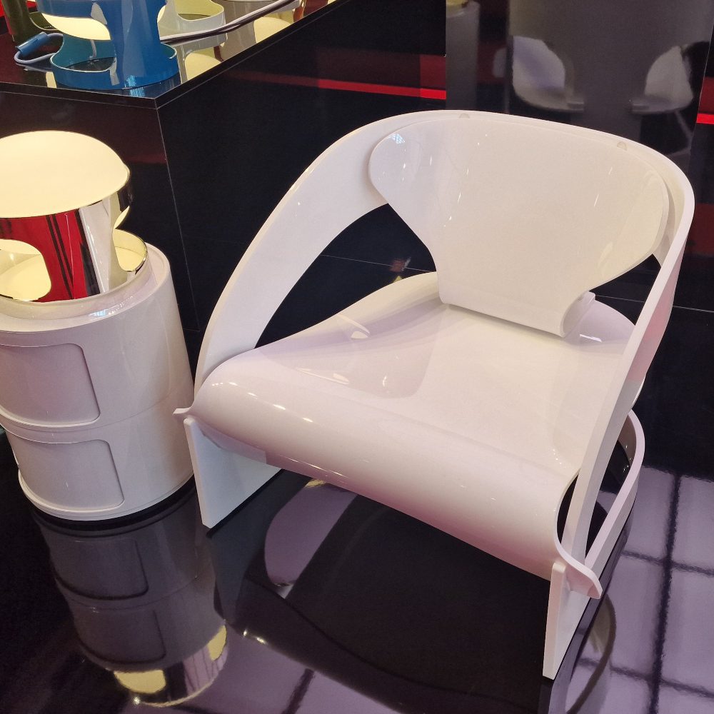 A minimalist white chair and lamp contrast against a bold black floor, showcasing a chic and contemporary design. The chair has a glossy touch, one of the trends seen at salone del mobile 2025.