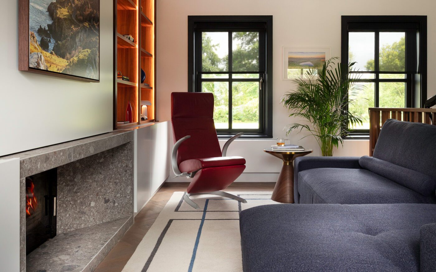 edit design studio project with edward sofa (1) A warm living room scene with a navy blue modular sofa, a red armchair, a fireplace, and an artistic painting above the mantel.