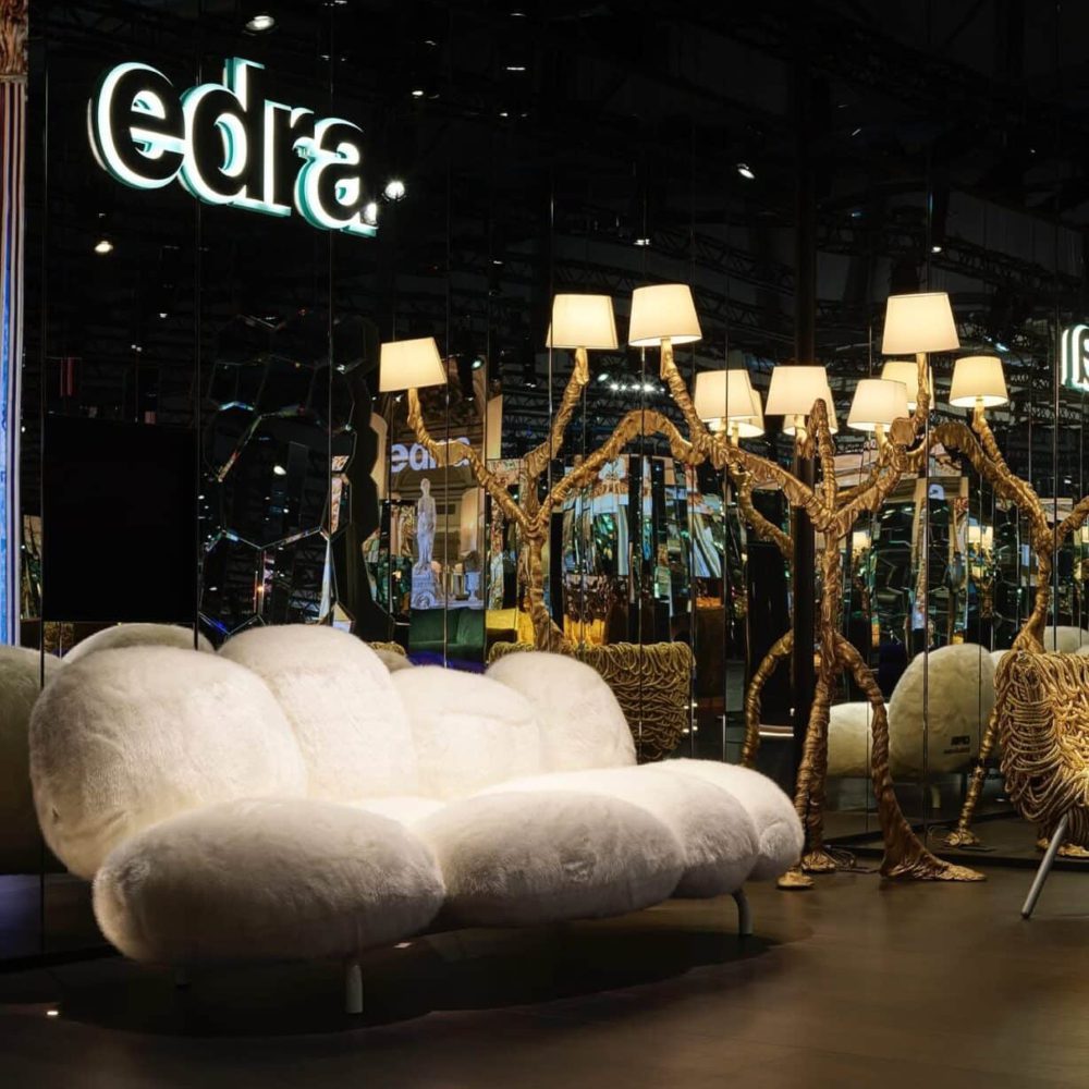 Round sofa upholstered in white with a gold lamp by its side.