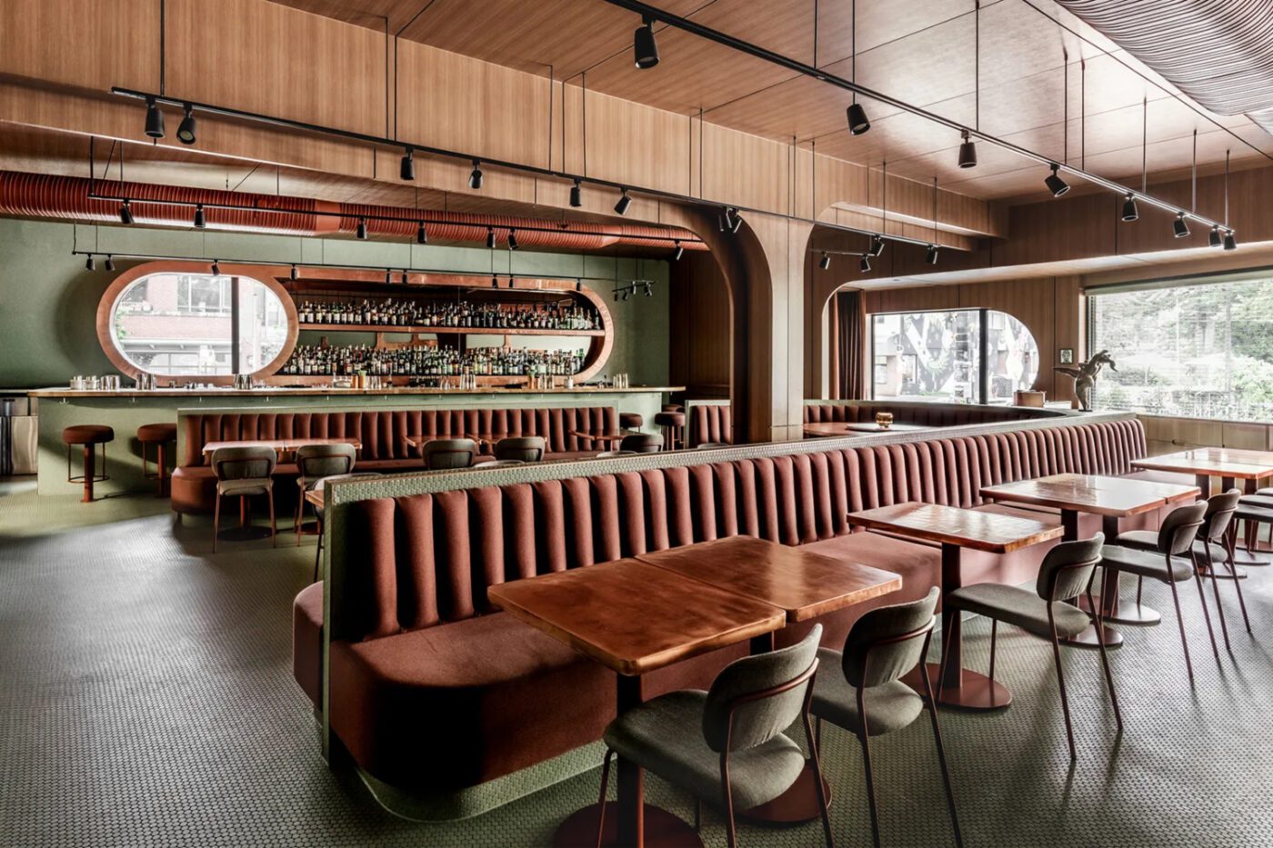 Stylish, modern restaurant interior with wooden panelling, long upholstered banquettes, round tables, and a sleek bar with shelves of bottles. Cosy and inviting. Designed by one of the best mexican interior designers.