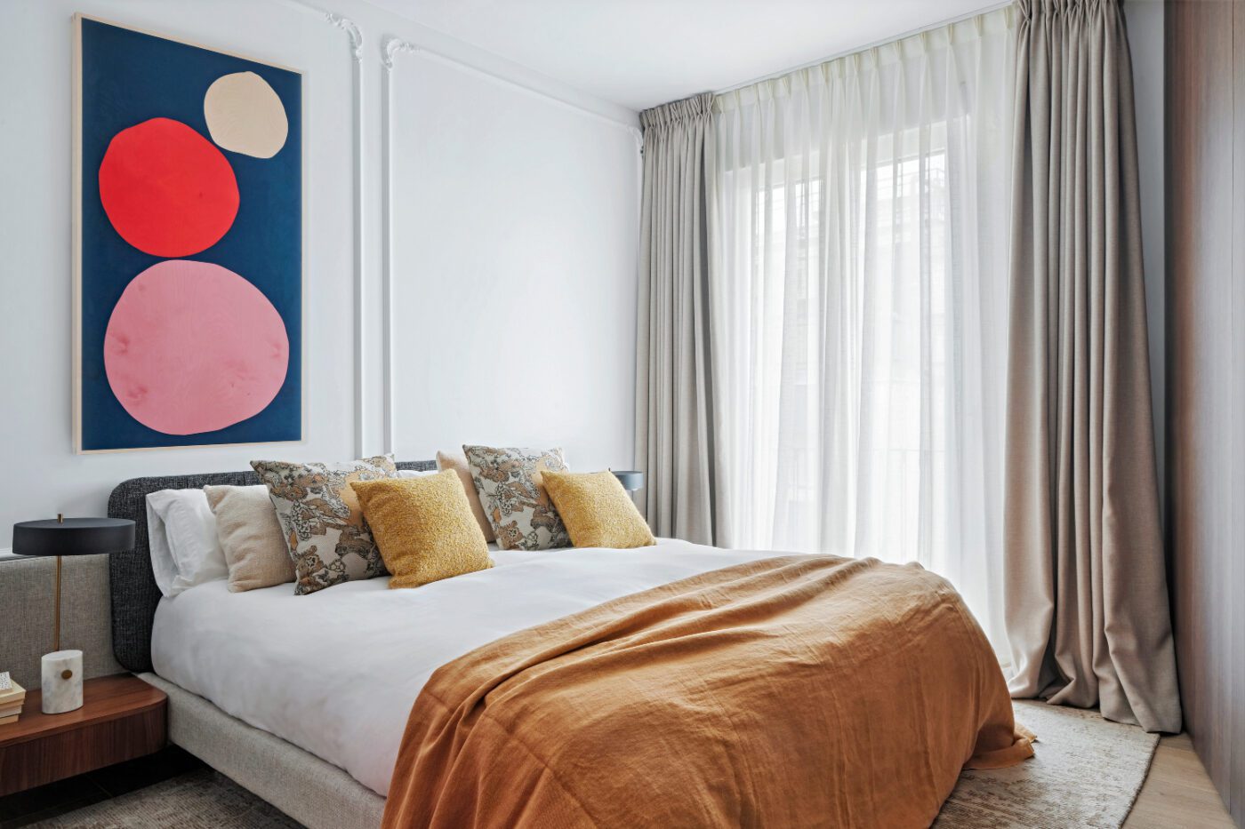 gulla5614r Modern bedroom with a large abstract painting featuring red and pink circles on a blue background. Neutral tones, soft lighting, and cosy bedding. By Blanca Rosa Gutiérrez