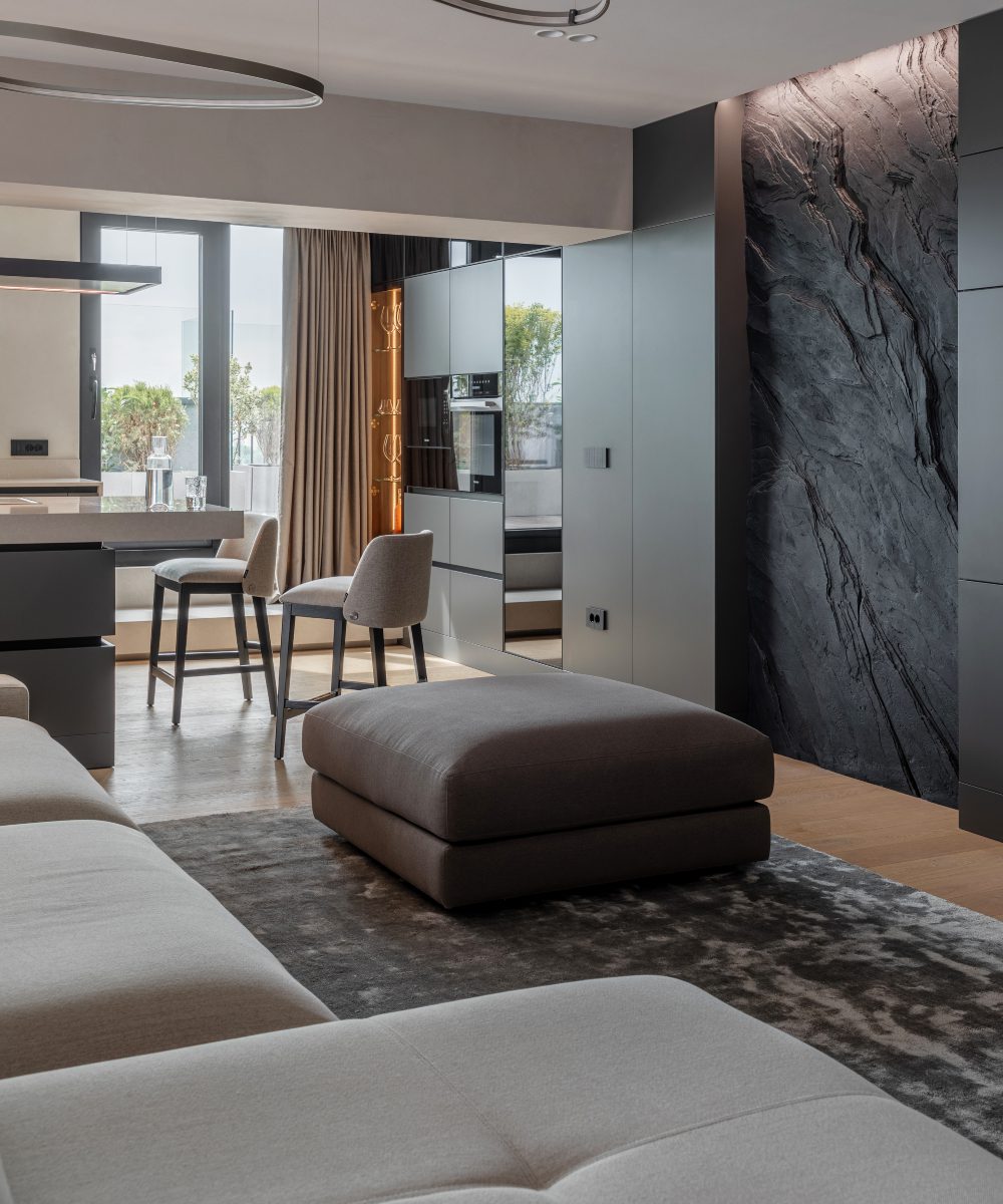 kitchen design by apunct studio Spacious modern living room and kitchen showcasing a striking stone wall, complemented by chic decor and ample natural light.