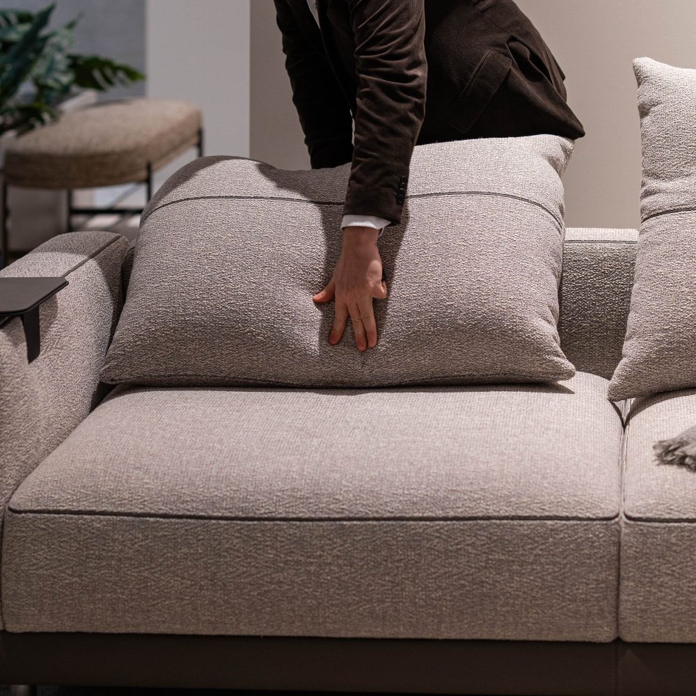 A man interacts with a couch, feeling its surface and assessing its style. He is also adjusting the cushion of the sofa. Seen at salone del mobile 2025.