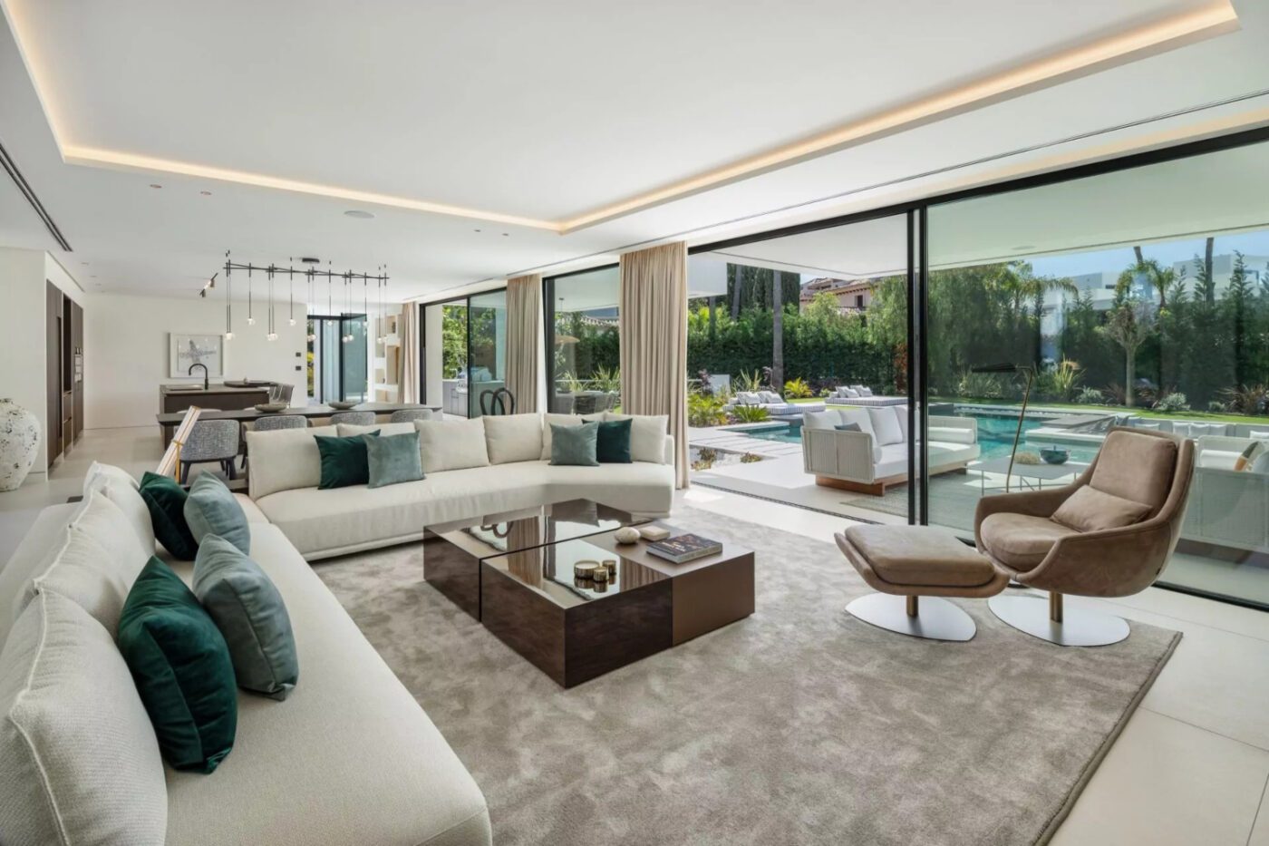 villa atalaya by blanca pera with Elba Spacious modern living room with expansive windows, showcasing a view of a serene pool outside. By Blanca Pera with Elba Armchair in brown velvet.