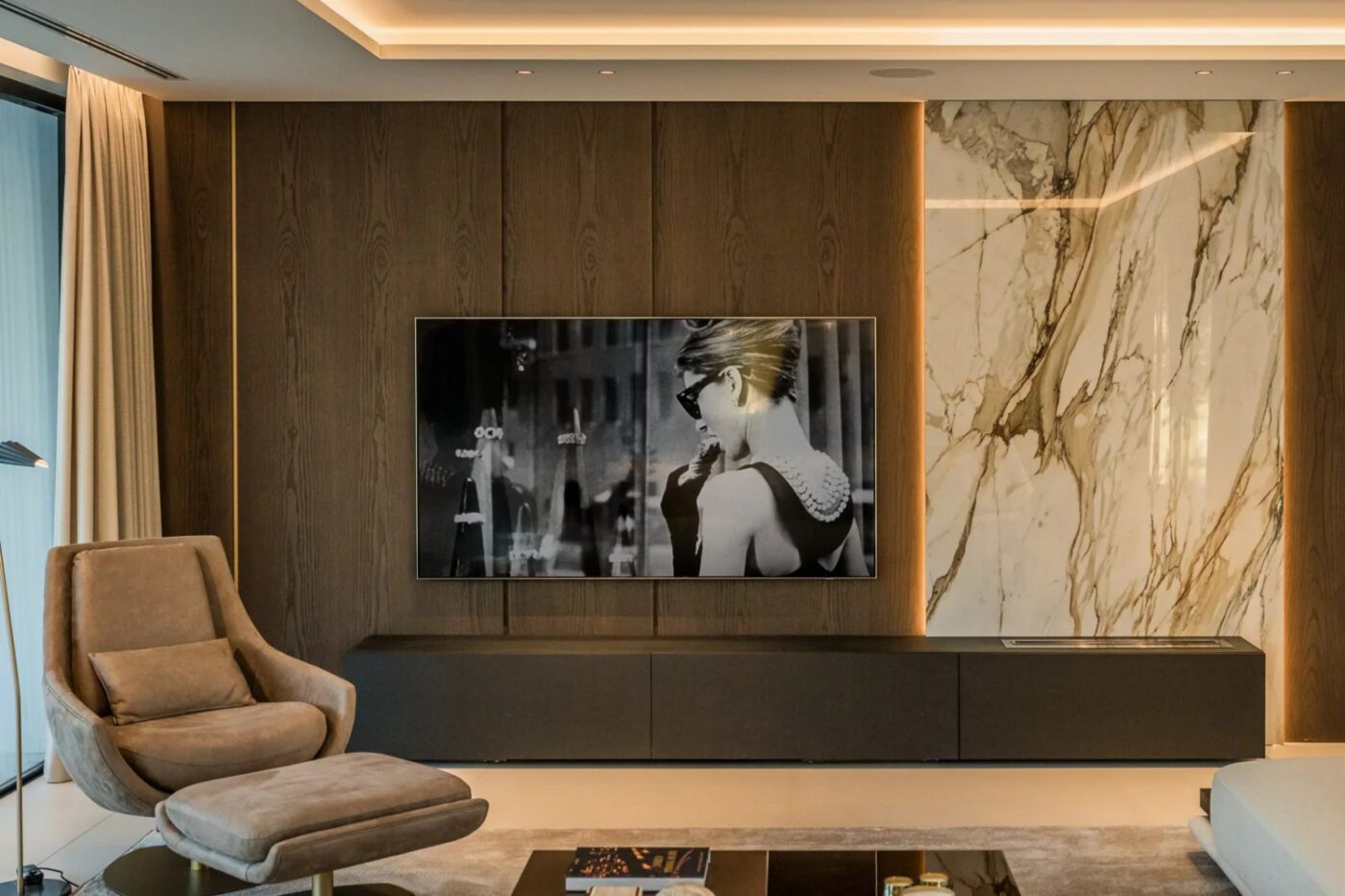 villa atalaya project with elba armchair Contemporary living room with elegant marble walls and a spacious television setup. By Blanca Pera with Elba Armchair in velvet brown.